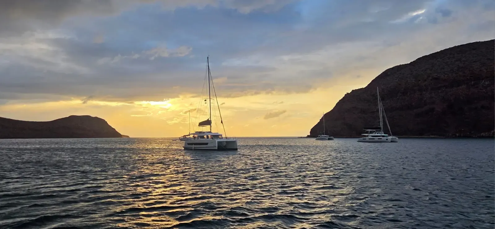 Catamaranes fondeados en una cala al atardecer, entre dos promontorios