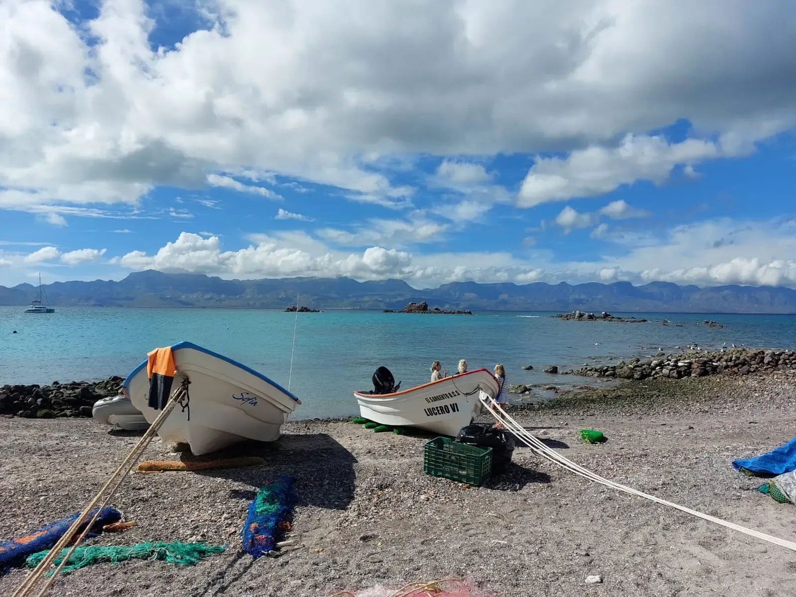 Barcas de pescadores varadas en una playa de piedras, con la bahía y las montañas al fondo