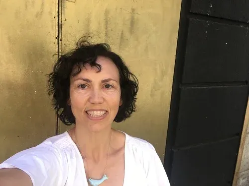 Belén González sonriente, con blusa blanca, delante de una puerta dorada