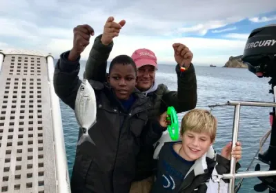 Dos niños y un adulto celebran a bordo de una lancha un pez recién pescado