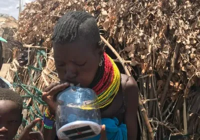 Una mujer turkana con collares de cuentas de colores bebe de una botella de plástico