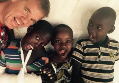 Un voluntario sonríe junto a tres niños, uno de ellos con el brazo vendado