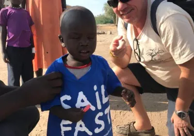 Un niño con una camiseta azul de «Sail fast» junto a un voluntario agachado