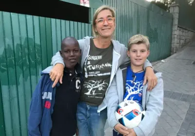 Una voluntaria con la camiseta de Cirugía en Turkana abraza a dos niños con un balón