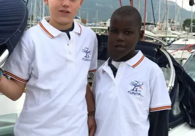 Dos niños con polos blancos de Turkana en un puerto, junto a los veleros