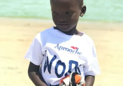 Un niño con una camiseta blanca de Aproache en la playa