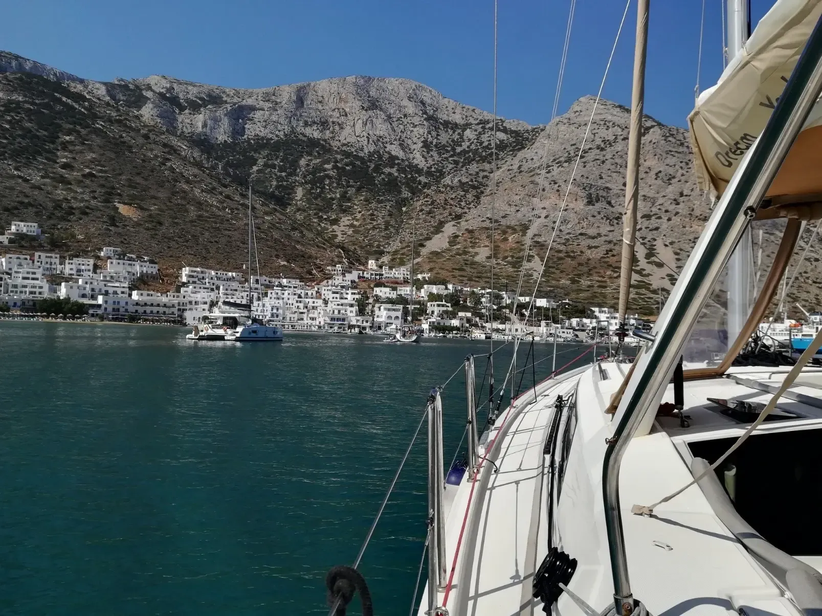 Pueblo blanco junto al puerto, al pie de unas montañas rocosas, visto desde la cubierta del velero