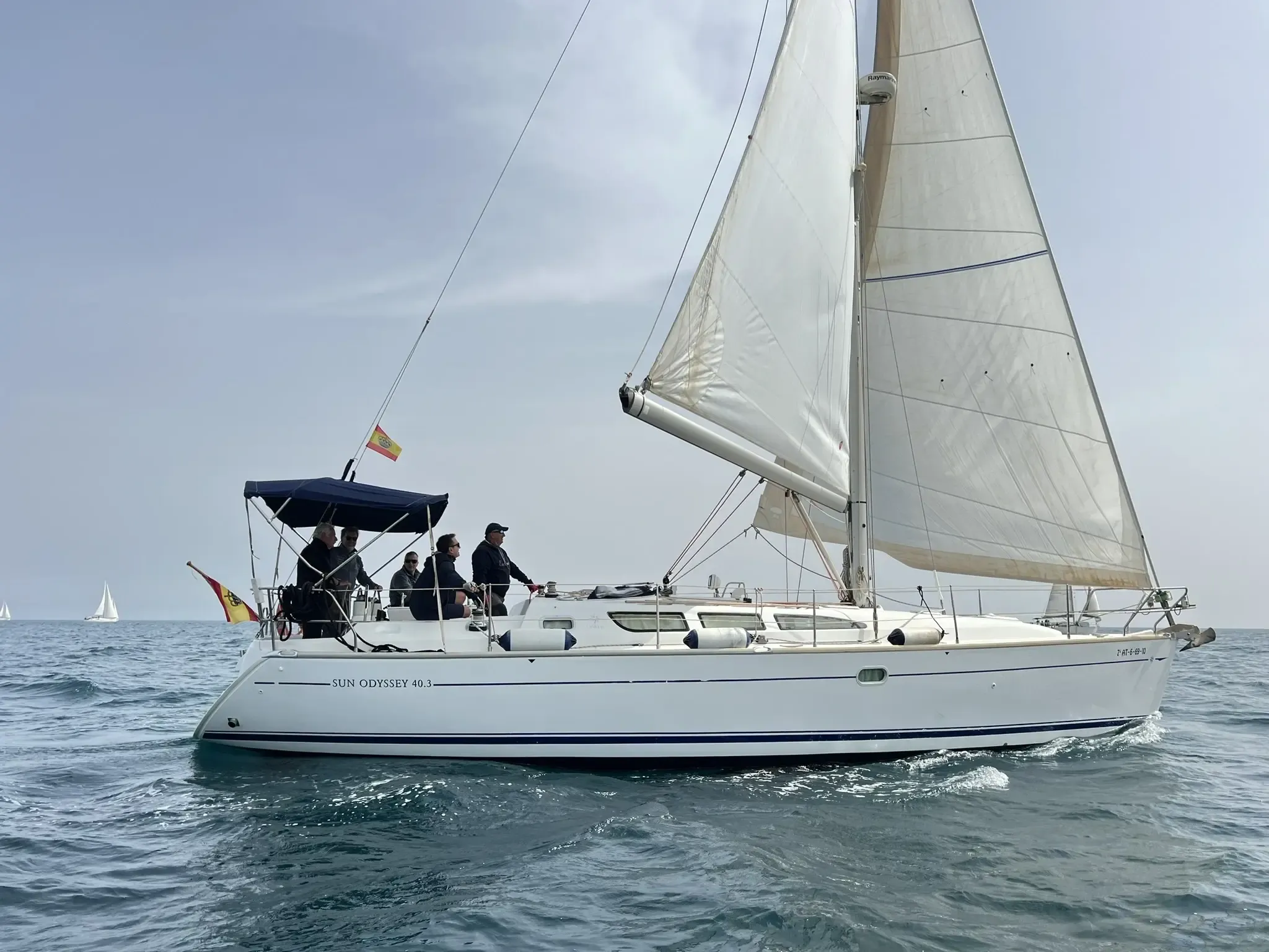 Velero con las velas desplegadas y la tripulación en la bañera, navegando con mar en calma